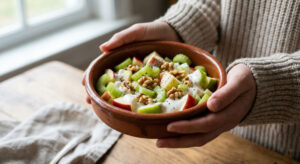 A close-up photograph of a person holding a bowl of fresh Vegetarian Apple and Walnut Salad with celery and yogurt dressing.