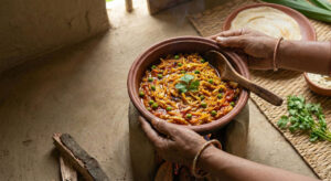 Woman holding a rustic clay pot filled with Bandhgobhi Hari Matar Tarkari, a shredded cabbage and green peas curry garnished with fresh cilantro.